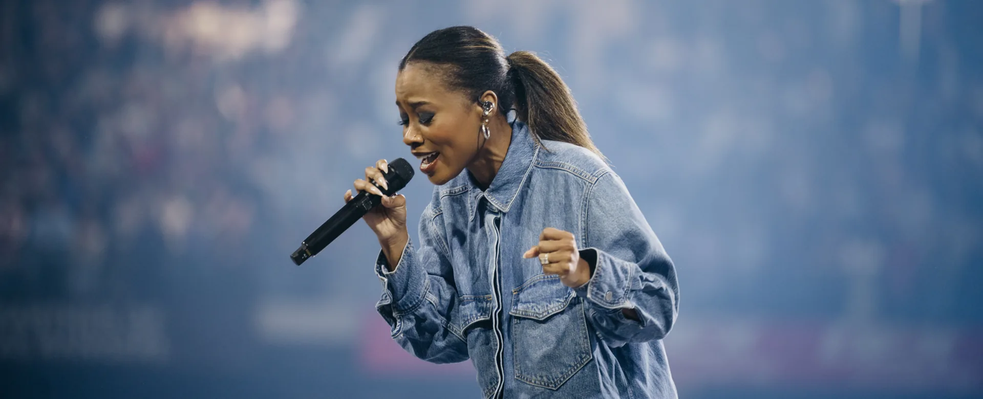 Worship leader singing into a microphone on stage in front of a blurred arena crowd